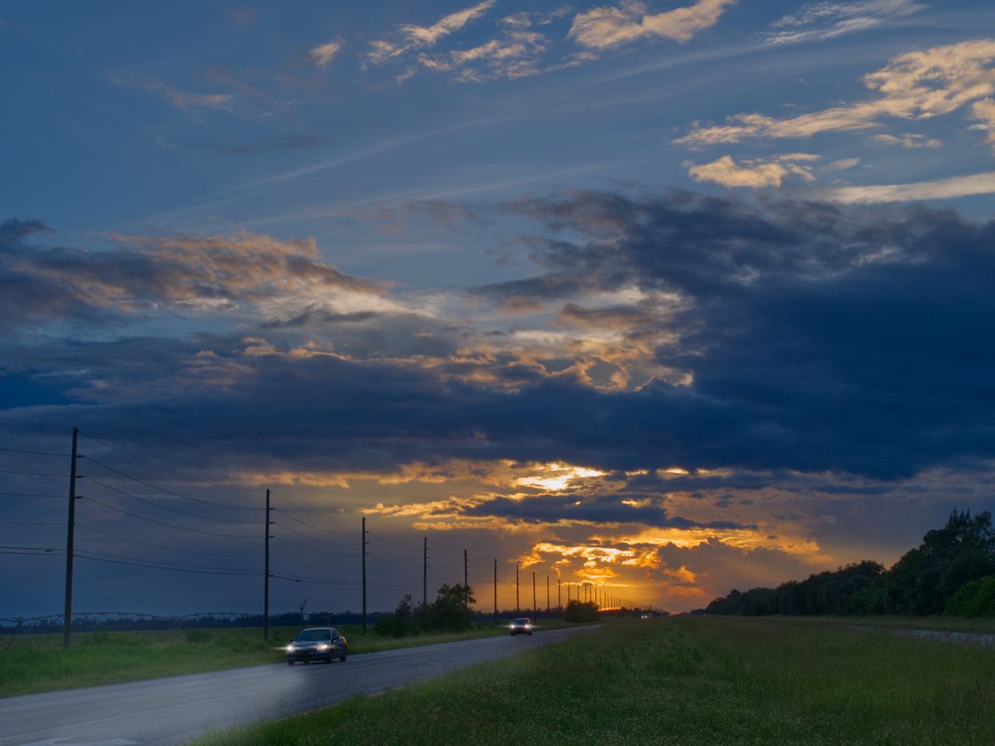 A two lane rural highway at dusk, headlights coming the other way under a break of gold in the clouds