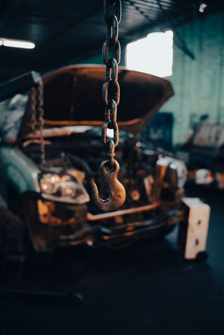 A chain and hook hanging in a workshop in front of a car with its hood raised