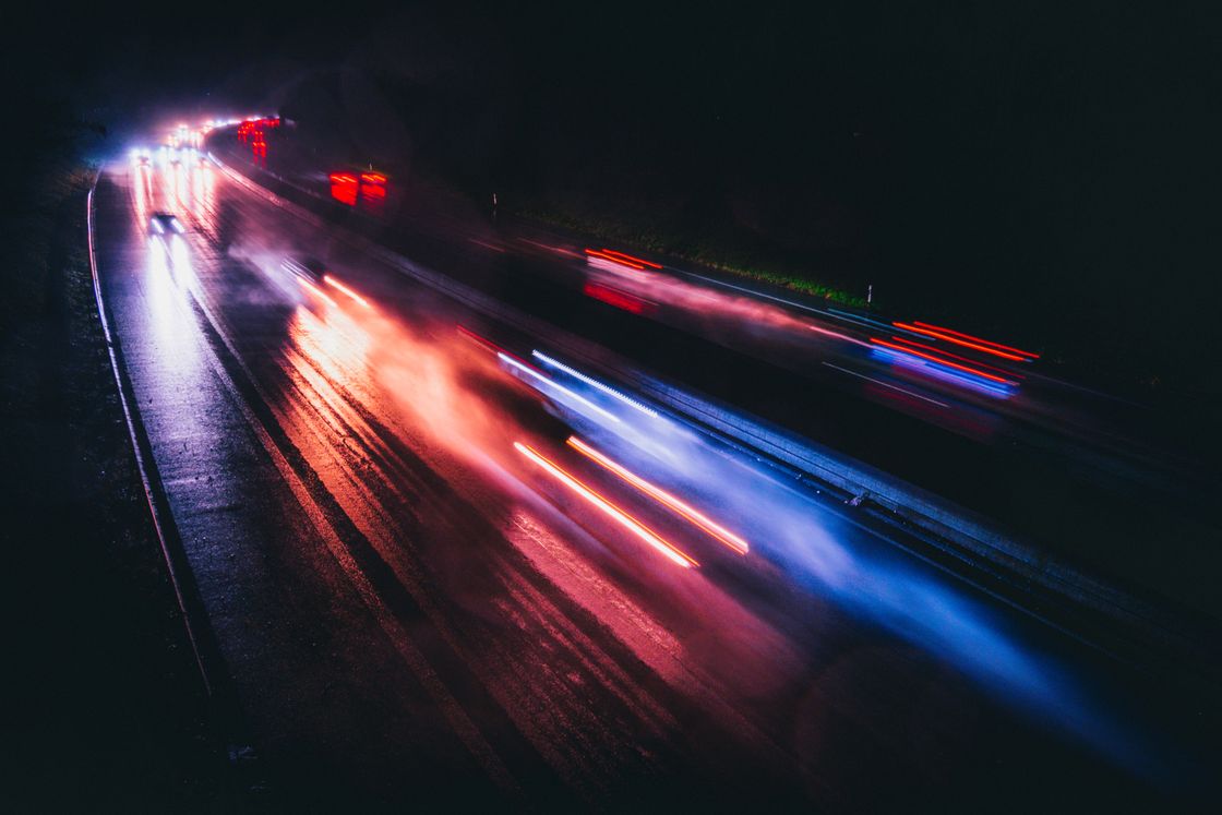 A long exposure of a wet highway at night, headlights and taillights drawn out into streaks across black asphalt