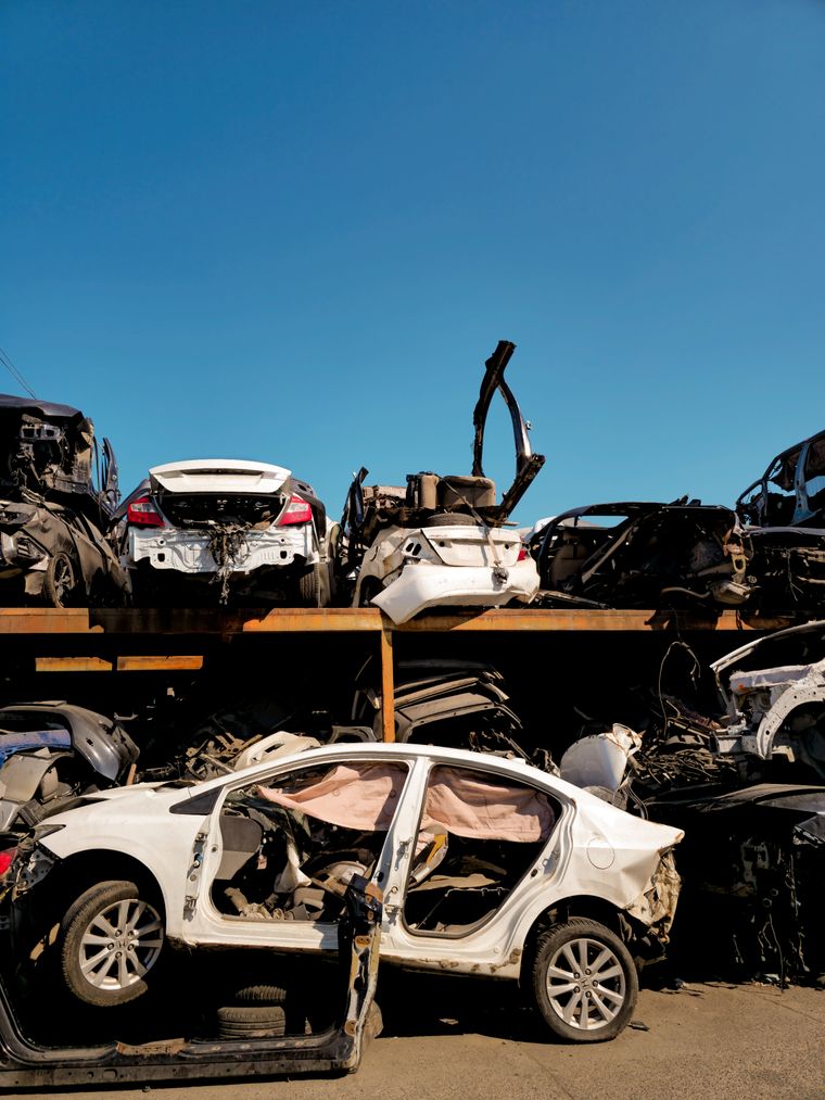 Rows of stripped cars racked two high in a salvage yard under a clear sky